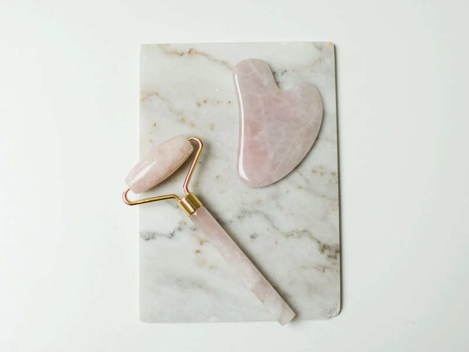Sfeerbeeld (niet de salon): Rozenkwarts gezichtsroller en gua sha op marmer