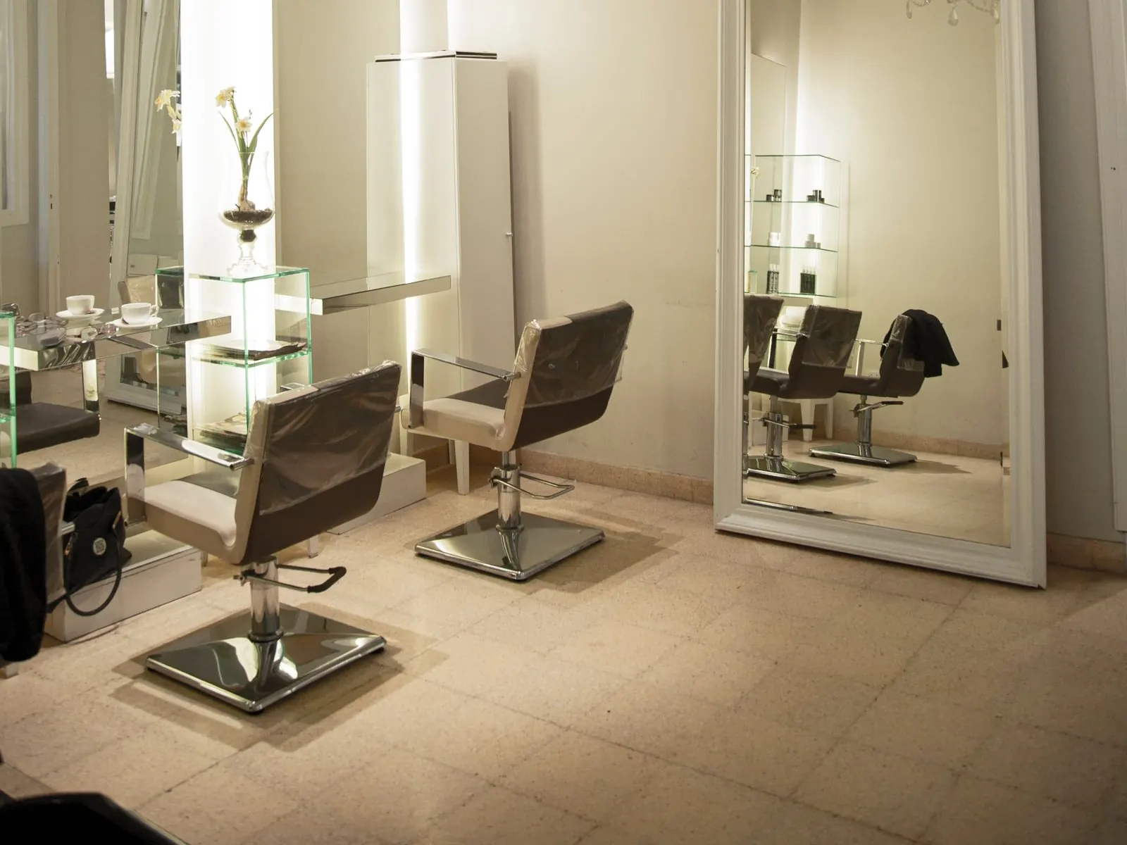 Sfeerbeeld (niet de salon): Lichte kapsalon met stoelen, grote spiegels en een kroonluchter