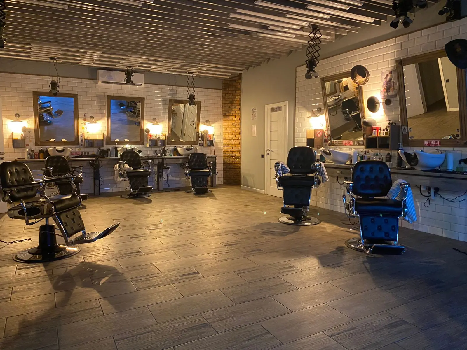 Sfeerbeeld (niet de salon): Schemerig kapsalon-interieur met stoelen en verlichte spiegels