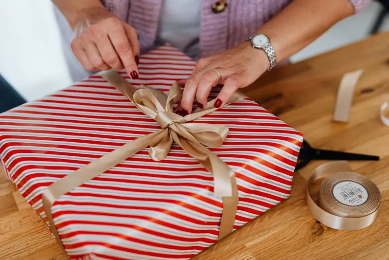 Handen strikken een goudkleurig lint om een cadeau in rood-wit gestreept papier.