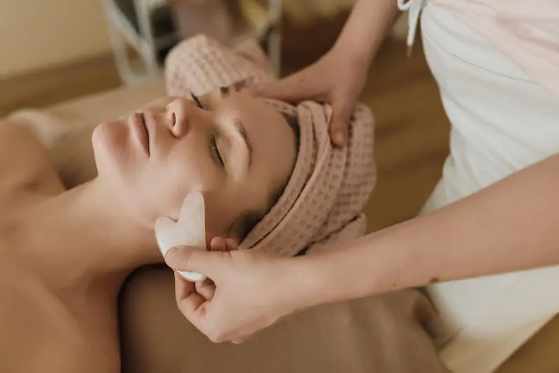 Schoonheidsspecialiste masseert het gezicht van een ontspannen klant met een gua sha-steen.