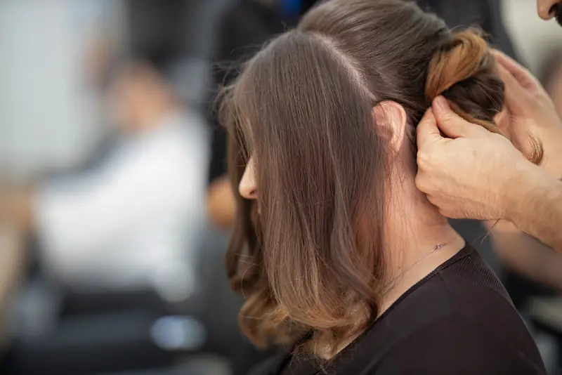 Kapper steekt het lange bruine haar van een klant op tijdens een stylingafspraak.