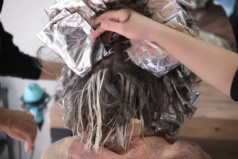 Kapster legt highlights met aluminiumfolie in het haar van een klant tijdens een kleurbehandeling.