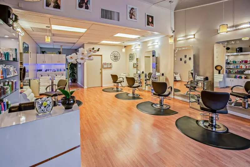 Ruime kapsalon met houten vloer, een rij kappersstoelen en schappen met haarproducten.