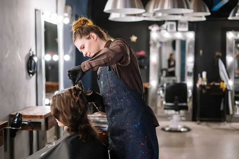 Kapster föhnt het haar van een klant in een salon met lampen en spiegels.