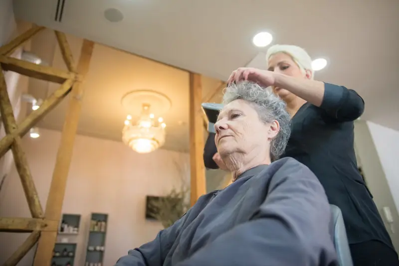 Kapster maakt het grijze haar van een oudere klant op in een salon met houten balken.