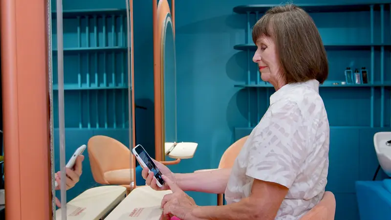 Klant in een kleurrijke salon kijkt op haar telefoon terwijl ze wacht op haar behandeling.