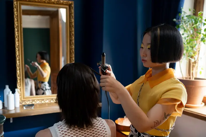 Stylist krult het haar van een klant met een krultang voor een vergulde spiegel.