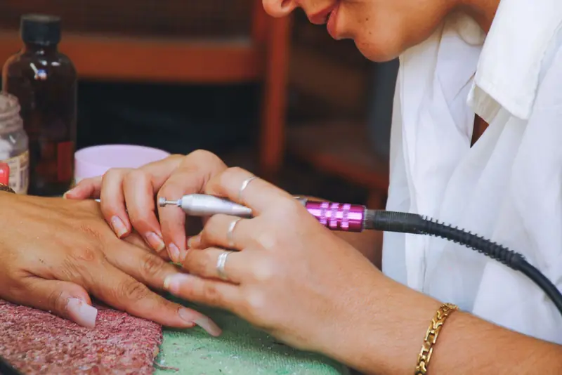 Nagelstyliste werkt de nagels van een klant bij met een elektrische nagelfrees.