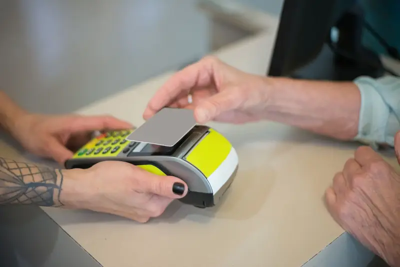 Klant houdt een pinpas tegen de betaalterminal die de medewerker aan de balie vasthoudt.