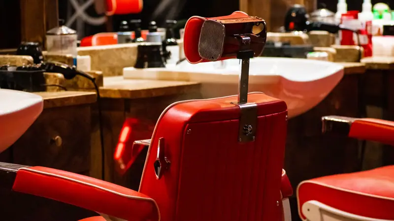 Lege rode kappersstoel voor een wasbak in een barbershop met houten werkplekken.