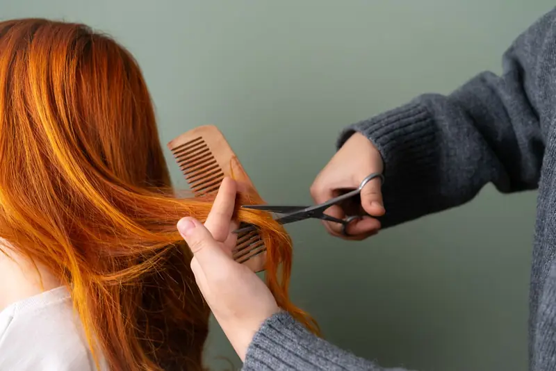 Kapper knipt de punten van lang rood haar met een houten kam en schaar.