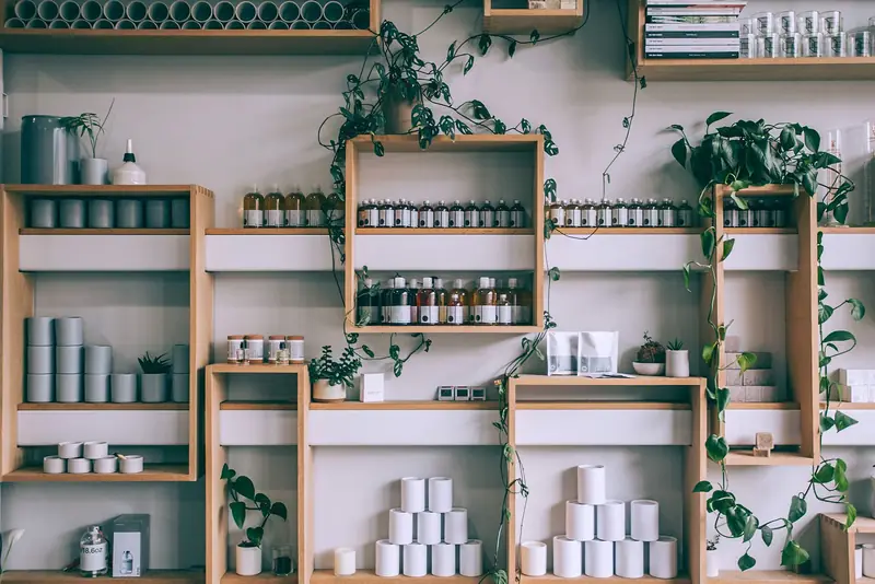 Houten wandschappen met flesjes, potjes en planten in een lichte winkel.